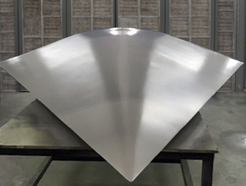 The completed RF test body is sitting on a table in a manufacturing bay. The aero-shaped structure has a matte silver finish.